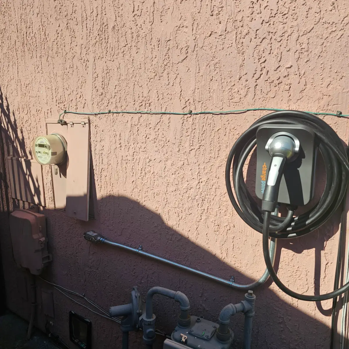 A wall-mounted ChargePoint electric vehicle charger with a coiled cable beside an electric meter and utility boxes on a pink stucco exterior wall.