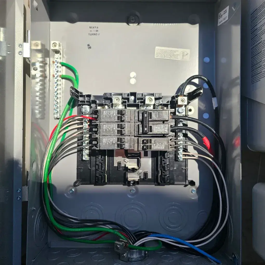 Open metal electrical panel with circuit breakers, terminal bars, and exposed green, black, white, red, and blue wiring.